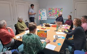 Members of the YellowYoYO discovery workshop site around a table with whiteboards and postit notes discussing ideas