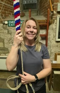 Gemma Groom, Marketing and Admin Officer stands smiling in a bell tower holding a bell rope.